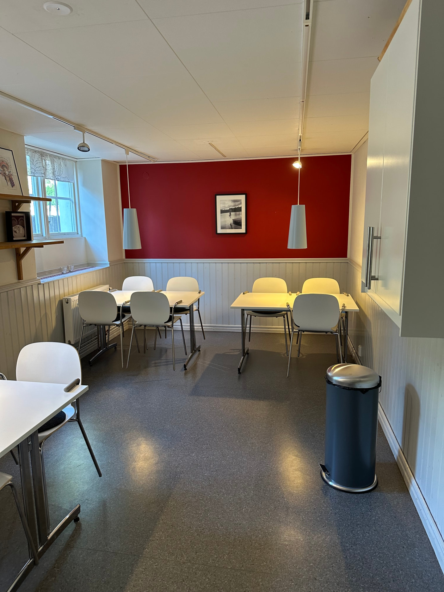 Gemensamt lunchrum med bord, stolar och röd accentvägg